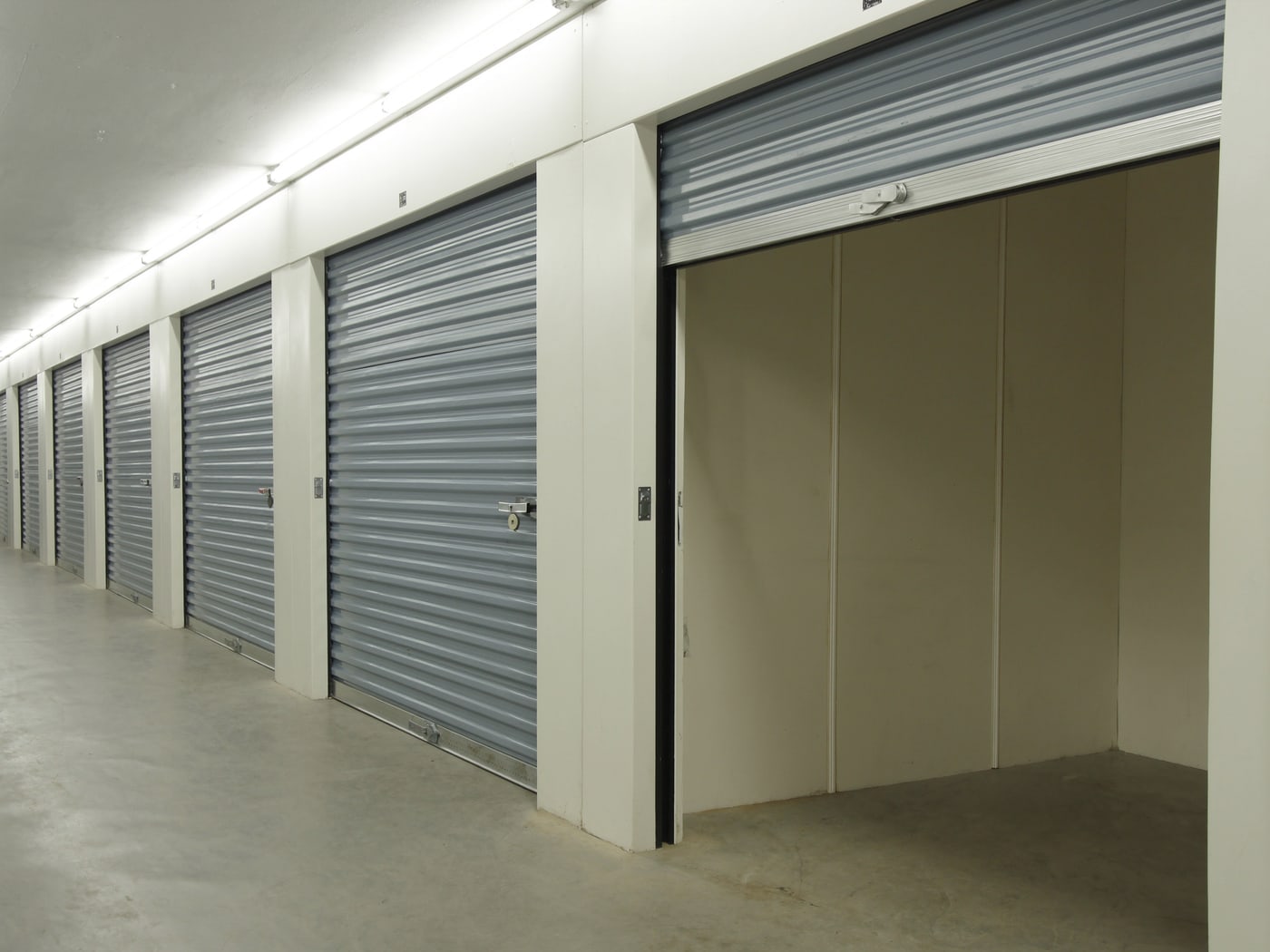 Row of modular storage units with steel roller doors, one unit open and empty